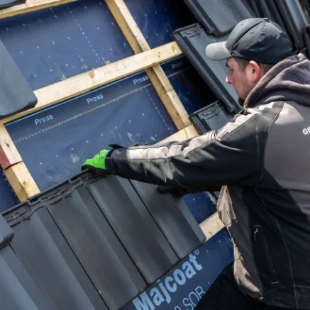 Dachdecker setzt einen Dachziegel auf die Dachlatten